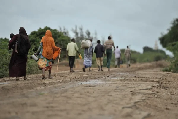 Climate Migration Explained: Why People Move and What Comes Next Displaced families carrying belongings walk along a dusty rural road in Somalia