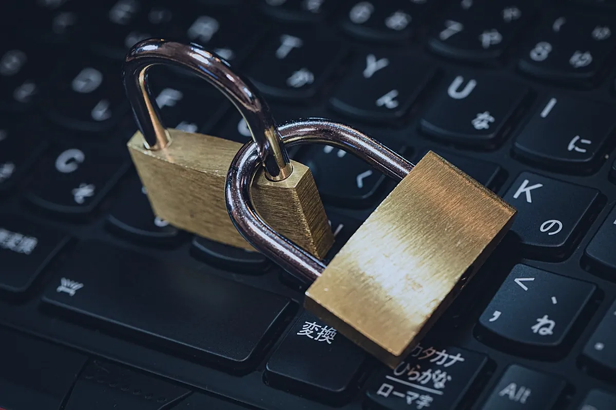 Two interlocked brass padlocks resting on a dark laptop keyboard, suggesting data security