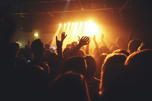 Excited concert crowd raising hands toward a glowing stage with warm lights