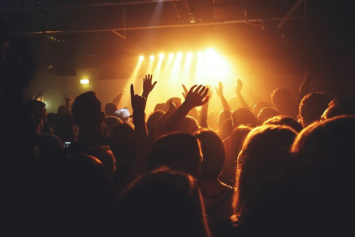 Excited concert crowd raising hands toward a glowing stage with warm lights