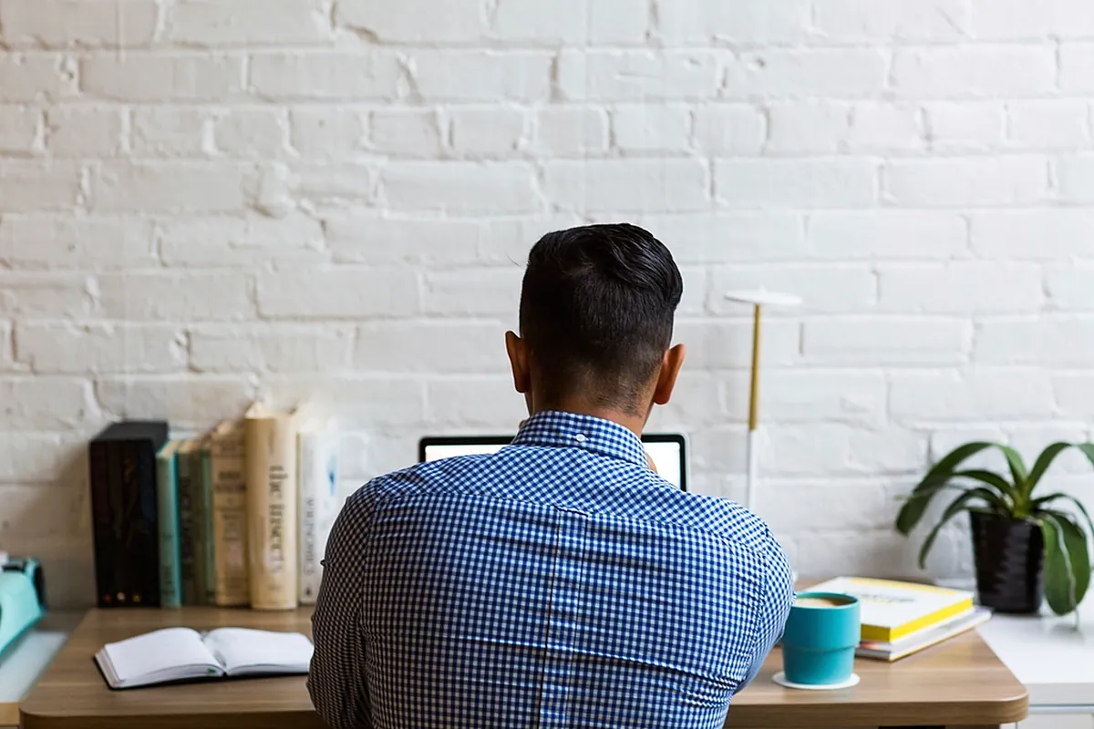 Man working remotely on a laptop at a bright home desk with books and plants