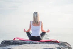 Woman meditating cross-legged on a seaside rock under a soft morning sky