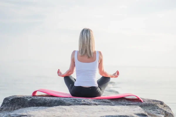 Sleep, Stress and Focus: Science-Backed Habits for Better Mental Health Woman meditating cross-legged on a seaside rock under a soft morning sky