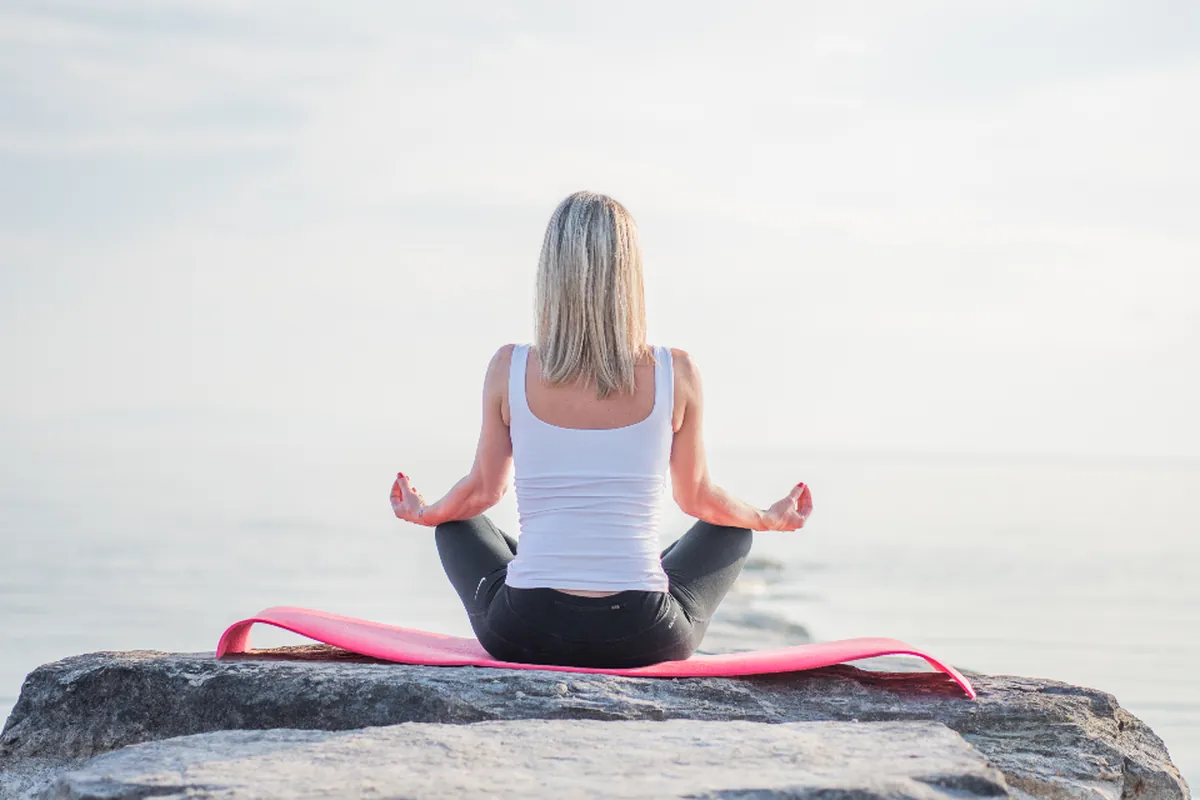 Woman meditating cross-legged on a seaside rock under a soft morning sky