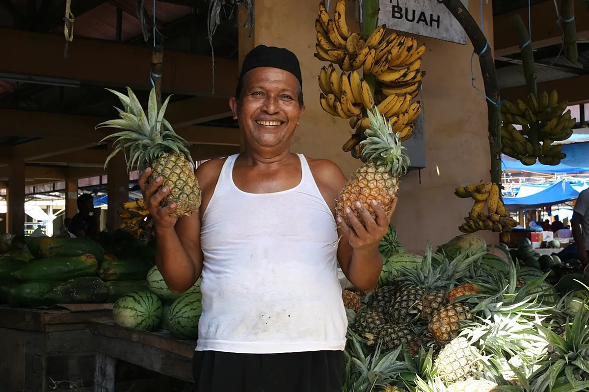 Smiling market stall owner holding fresh pineapples beside his fruit business