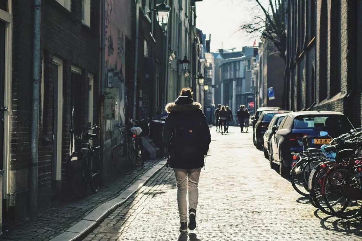 Street Style Around the World: How Cities Shape What We Wear Person in a dark coat walking down a sunlit cobblestone city street