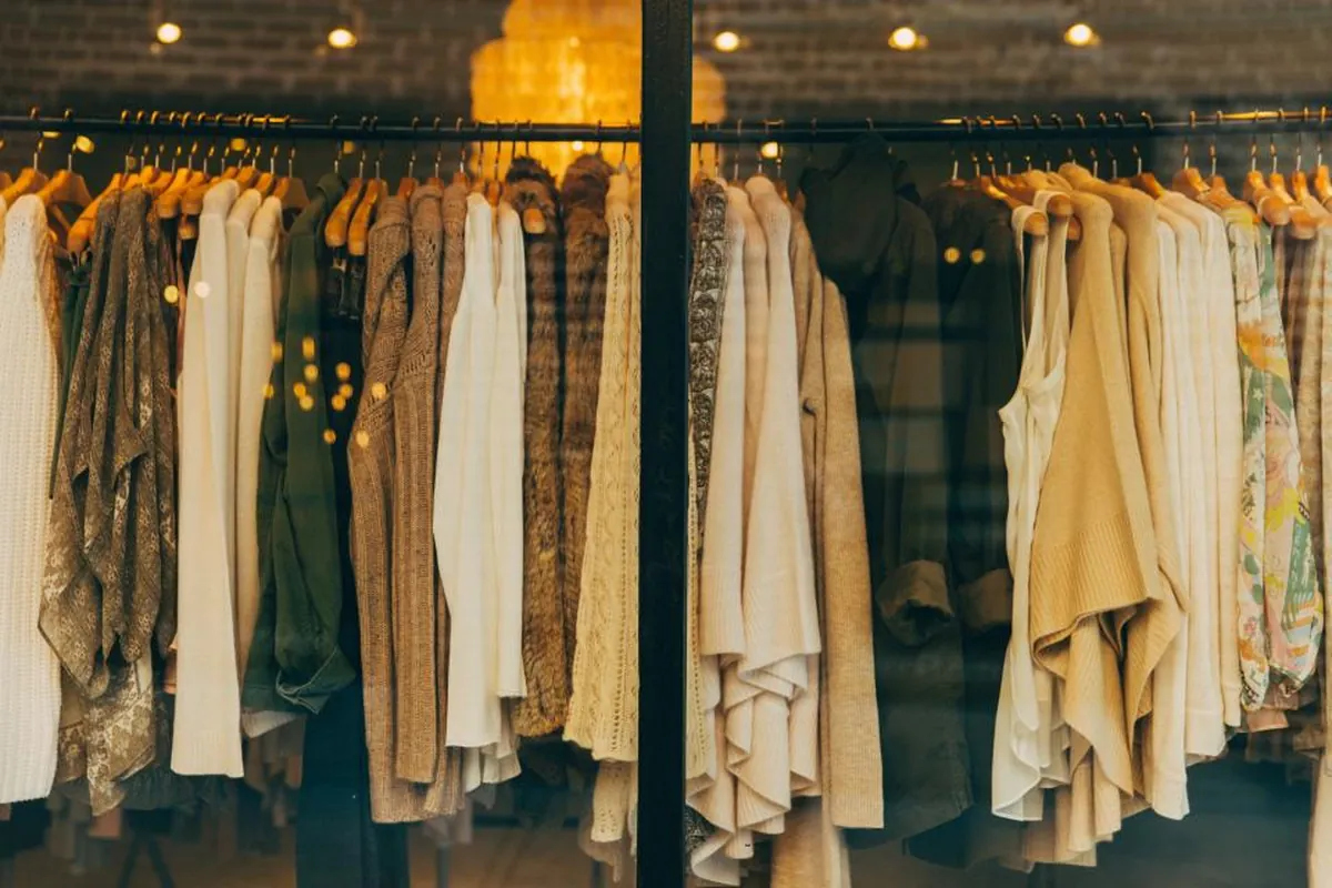 Rows of neutral-toned clothes hanging on racks in a warmly lit boutique